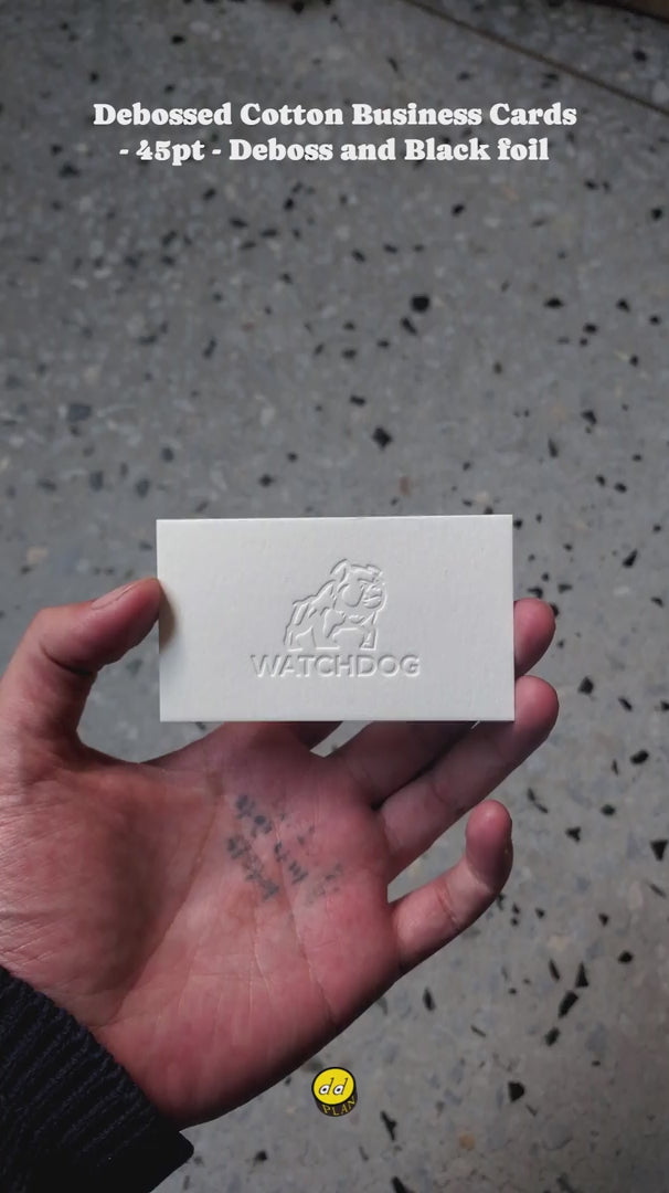 hand holding a 45pt cotton business card with recessed debossing and glossy black foil, showing thick edge and tactile texture.