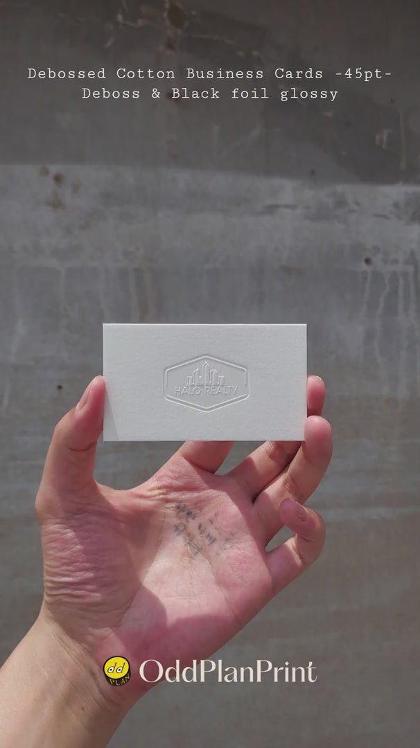 Luxury debossed cotton business cards 45pt thick showing tactile deboss and glossy black foil shine by OddPlanPrint.