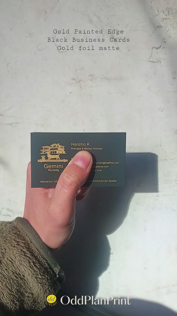 Premium black business cards with gold painted edges and matte gold foil stamping on thick stock, close-up stack showing luxurious shine and texture.