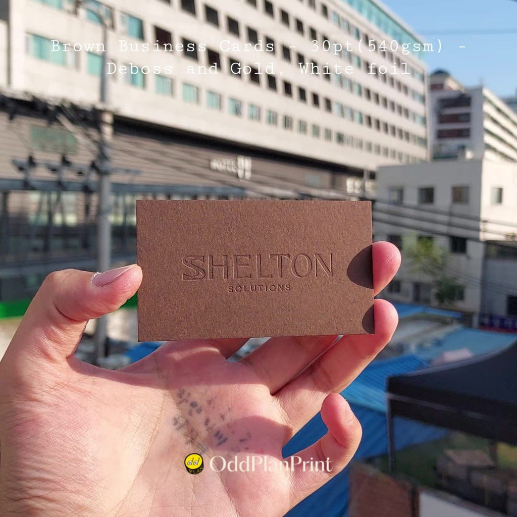 Grounded brown business cards use deboss, gold foil, and white foil by OddPlanPrint.