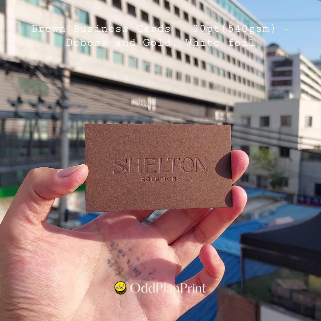 Grounded brown business cards use deboss, gold foil, and white foil by OddPlanPrint.