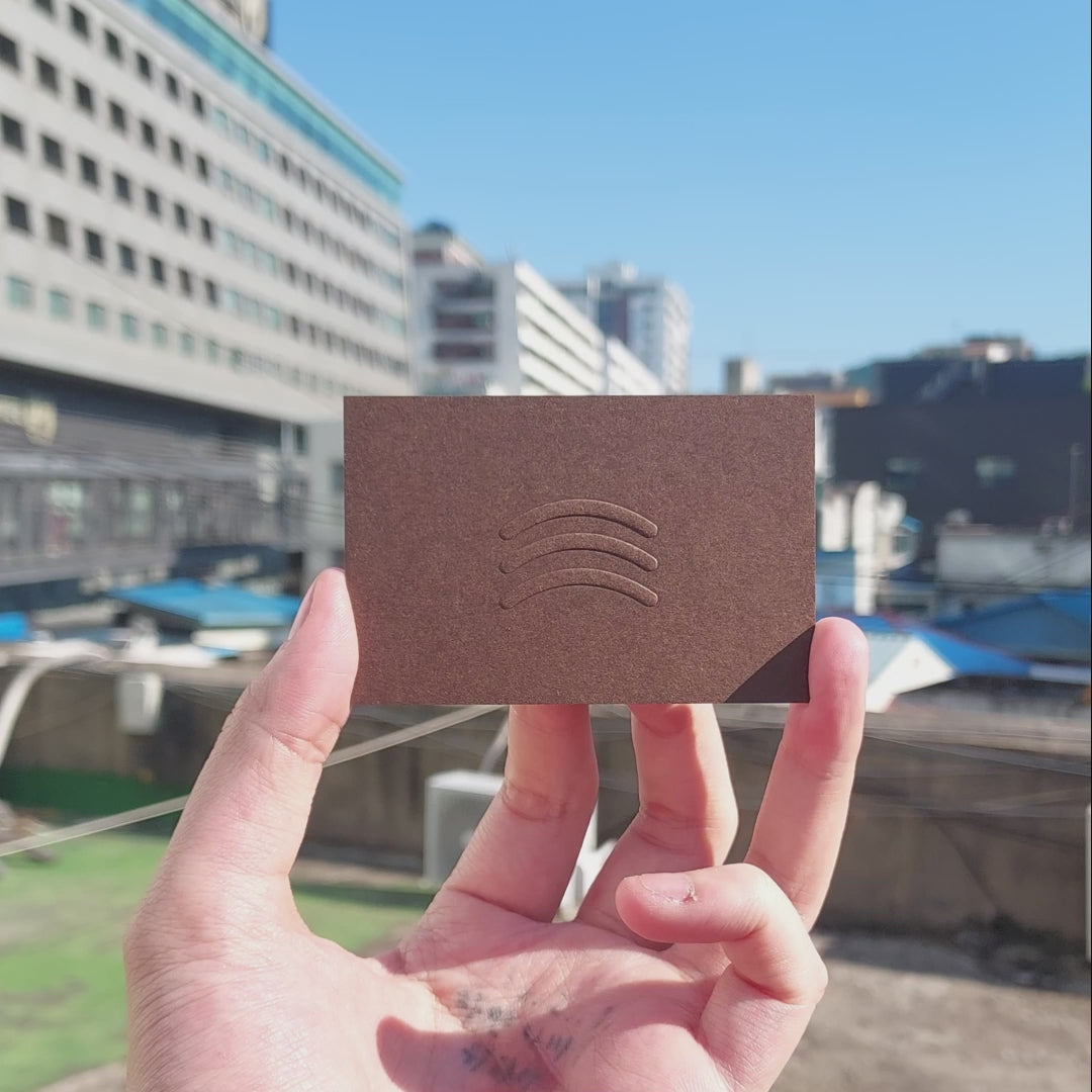 High-end brown business card with artisan embossing and foil detail.